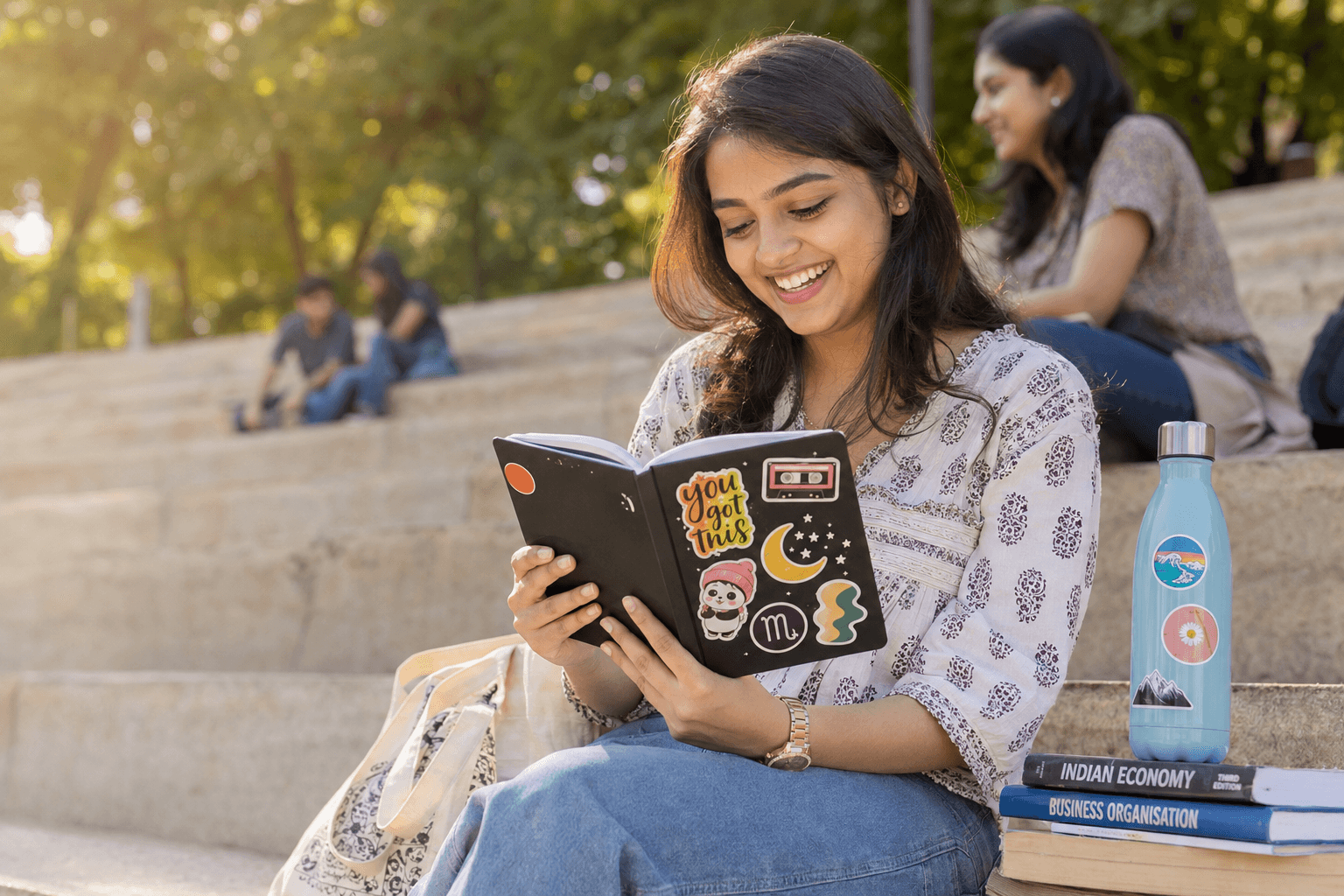 An Indian college student on campus steps, her diary and water bottle covered in stickers.